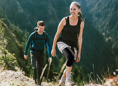 A man and woman wearing thigh sleeves hiking in a mountain
