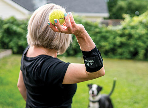 Woman wearing elbow band playing fetch with a dog