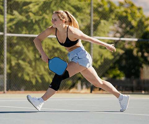 A woman playing pickleball while wearing a knee compression sleeve