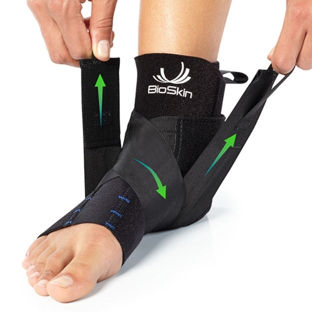 Close-up of left foot in ankle sleeve as two hands pull support straps upward; arrows indicate tightening steps.