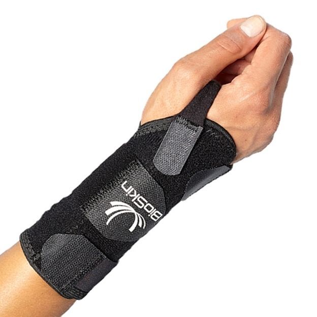 Black BioSkin wrist brace with thumb loop and adjustable straps, shown on a hand for wrist and thumb support.