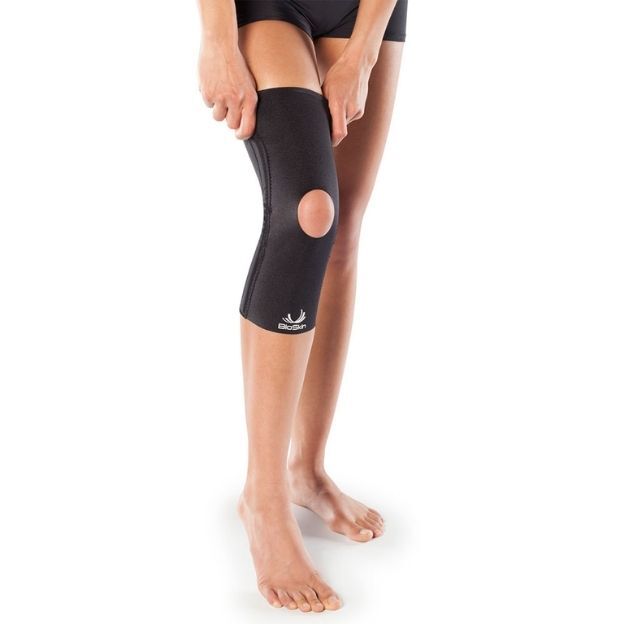 Person pulling on a black BioSkin open-patella knee sleeve for support, shown on a bare leg.