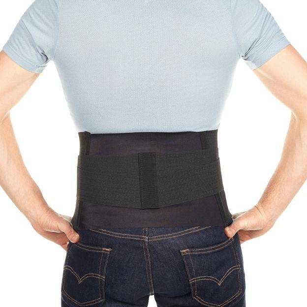 Back view of person in light blue shirt wearing a black lumbar support belt over jeans, hands on hips.