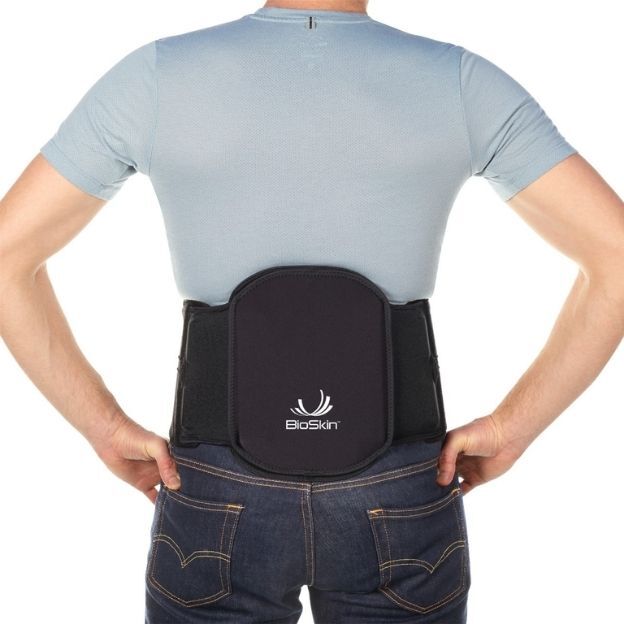 Back view of person wearing a black Vector Lumbar Support brace over a light blue shirt, hands on hips.