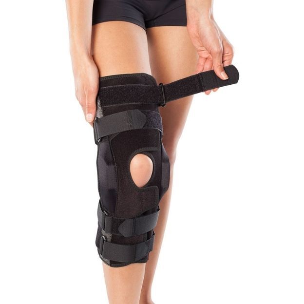 Close-up of a leg wearing a Bodyguard Wraparound brace; user secures the top strap above an open patella ring for support.